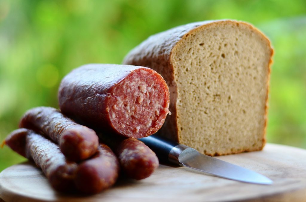 Fleisch & Wurst Großhandel. Jausenwurst auf eiem Holzbrett mit einem angeschnittenen Laib Brot